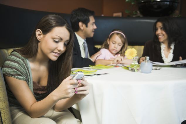 Family in restaurant, teenage girl (14-16) reading text message